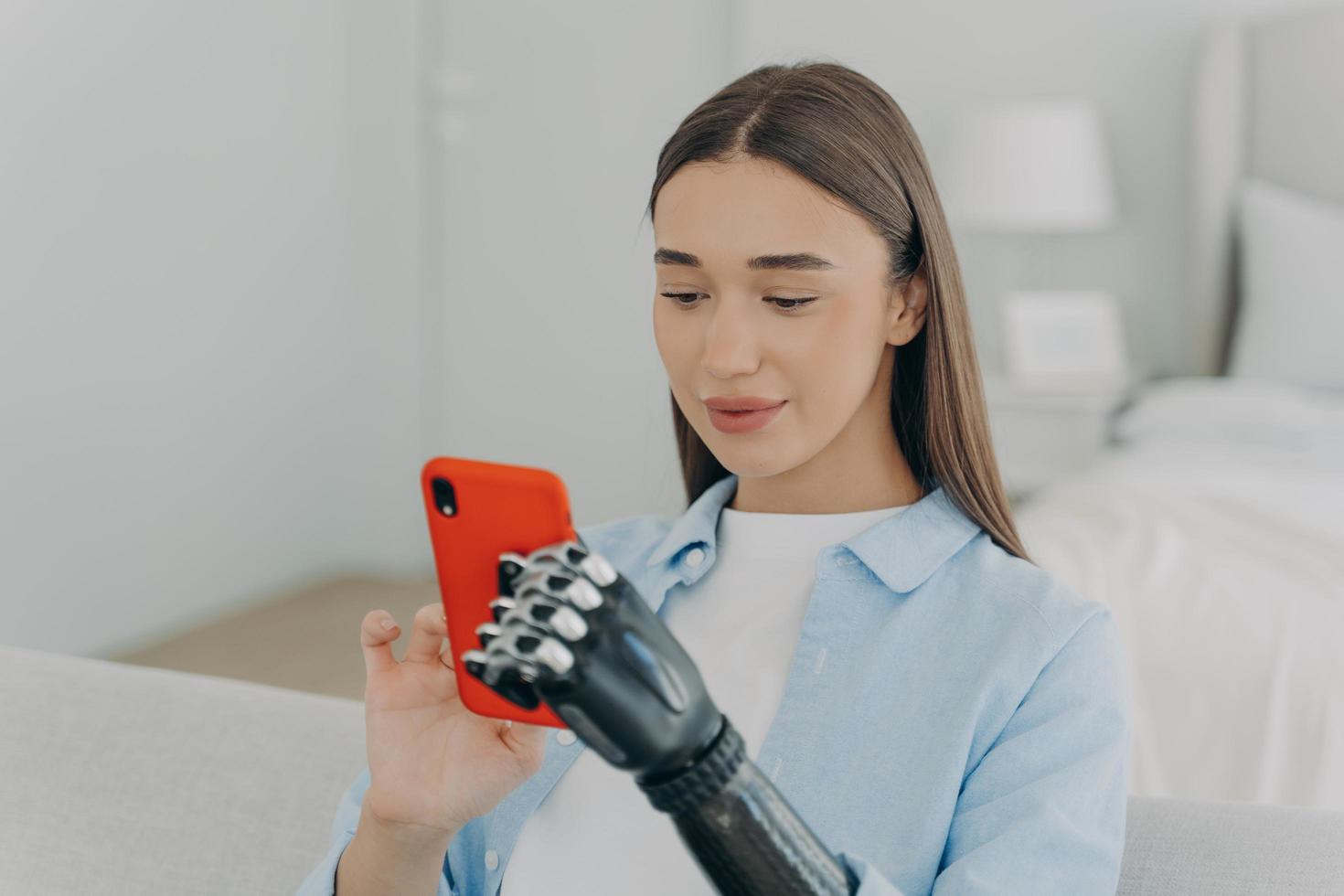 Happy disabled young girl with bionic arm prosthesis holding smartphone, shopping in online store photo