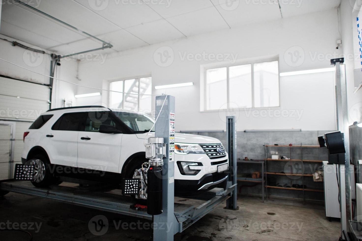 coche todoterreno americano en soporte para verificación de inclinación de alineación de ruedas en el taller de la estación de servicio. foto