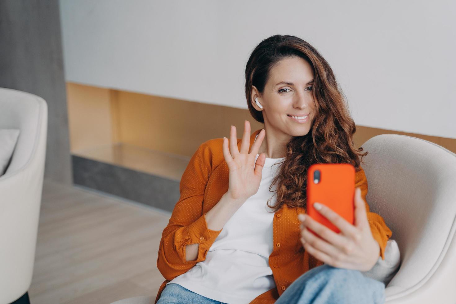 Smiling female blogger in earphones answer video call on phone, waving hand, greeting followers photo