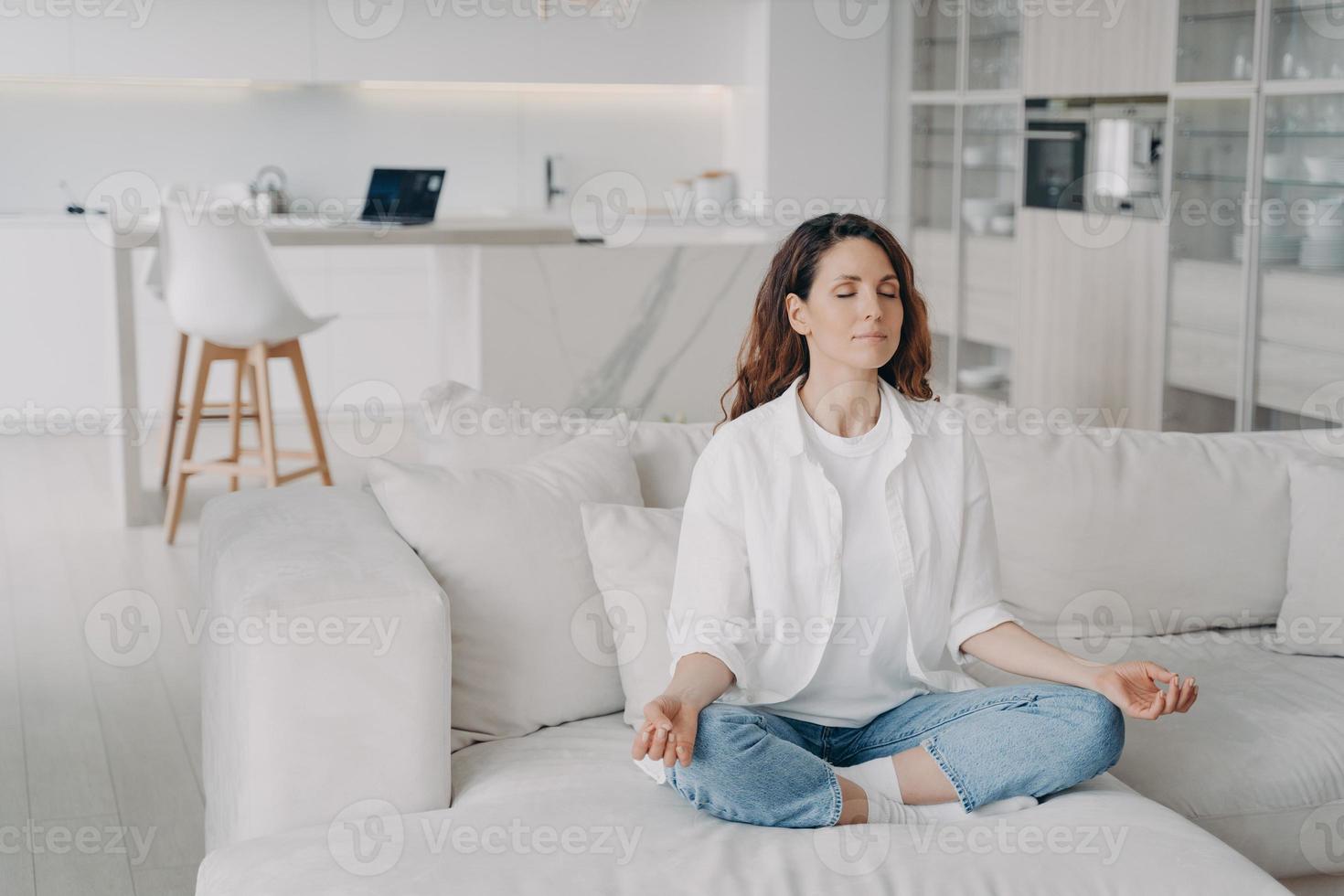 mujer hispana practicando yoga, medita, haciendo ejercicios de respiración en un cómodo sofá en casa foto