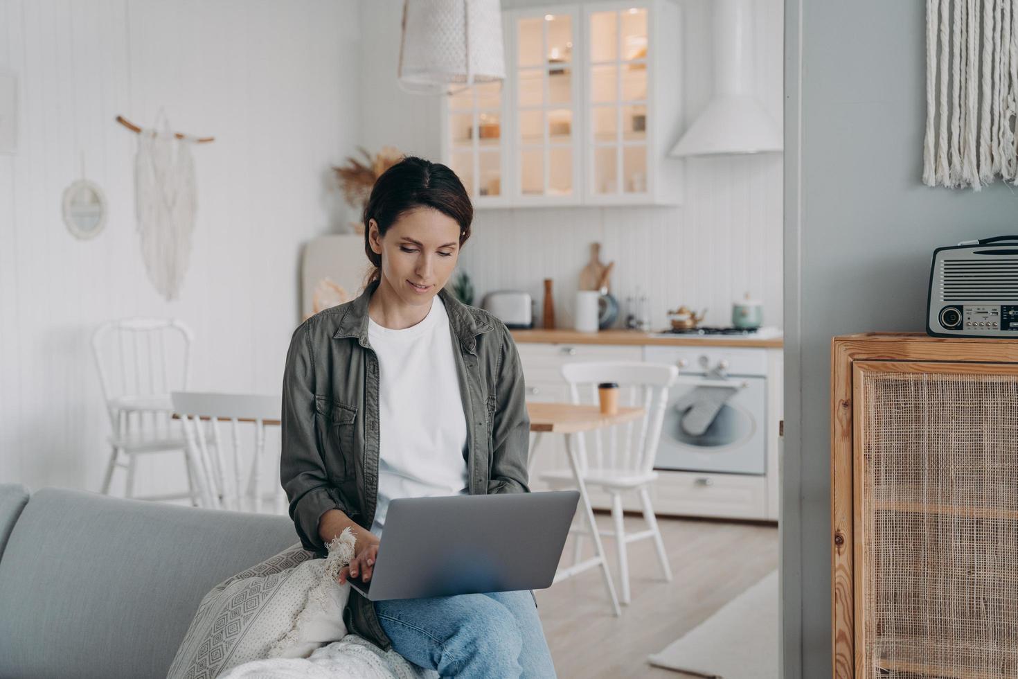 mujer usando laptop, comprando o trabajando en línea, chateando en redes sociales, sentada en un sofá en casa foto