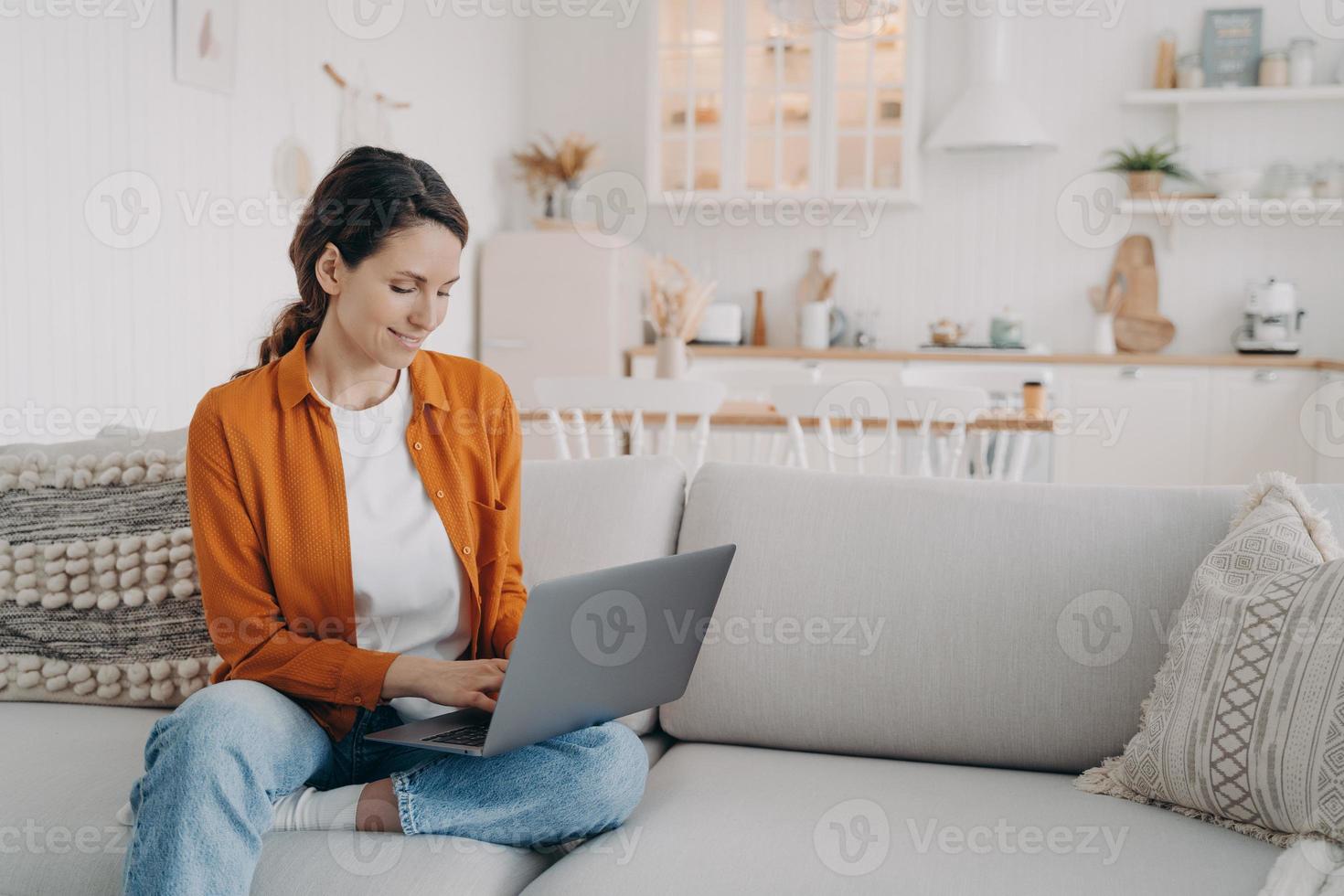 chica moderna trabajando en una laptop, comprando en línea, chateando en las redes sociales, sentada en un sofá en casa foto