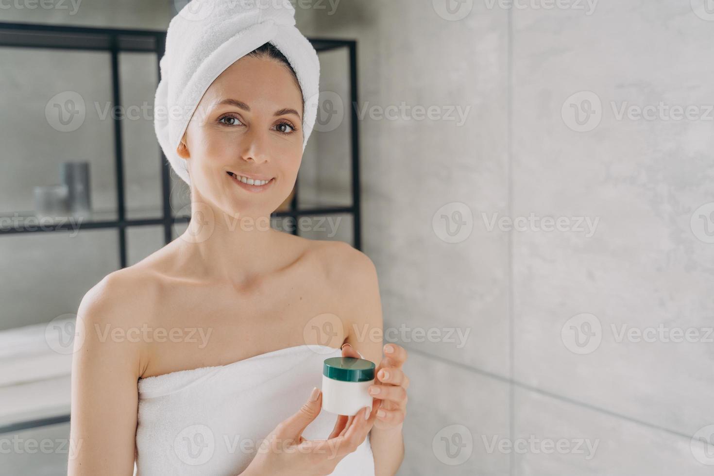 mujer sosteniendo un tarro de cosméticos de maqueta con crema, anunciando un producto de belleza para el cuidado de la piel en el baño foto