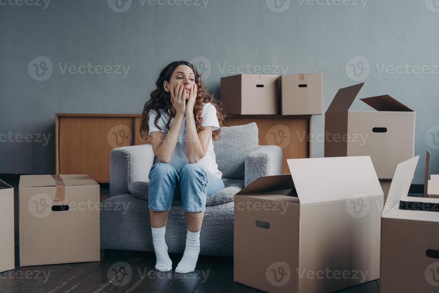 Tired divorced girl sitting with cardboard boxes on relocation day. Moving to rented house, eviction photo