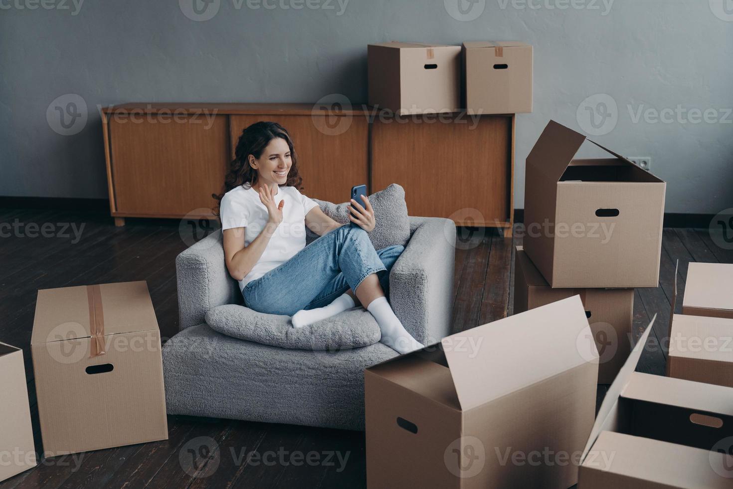 chica bloguera saludando a sus seguidores en las redes sociales, sentada con cajas para reubicarse el día de la mudanza foto