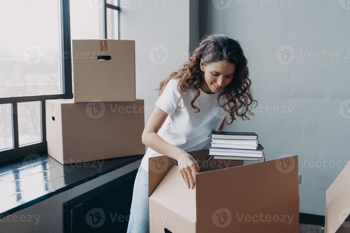 Happy woman packing carton box with things, relocating in new home. Moving, real estate rental photo