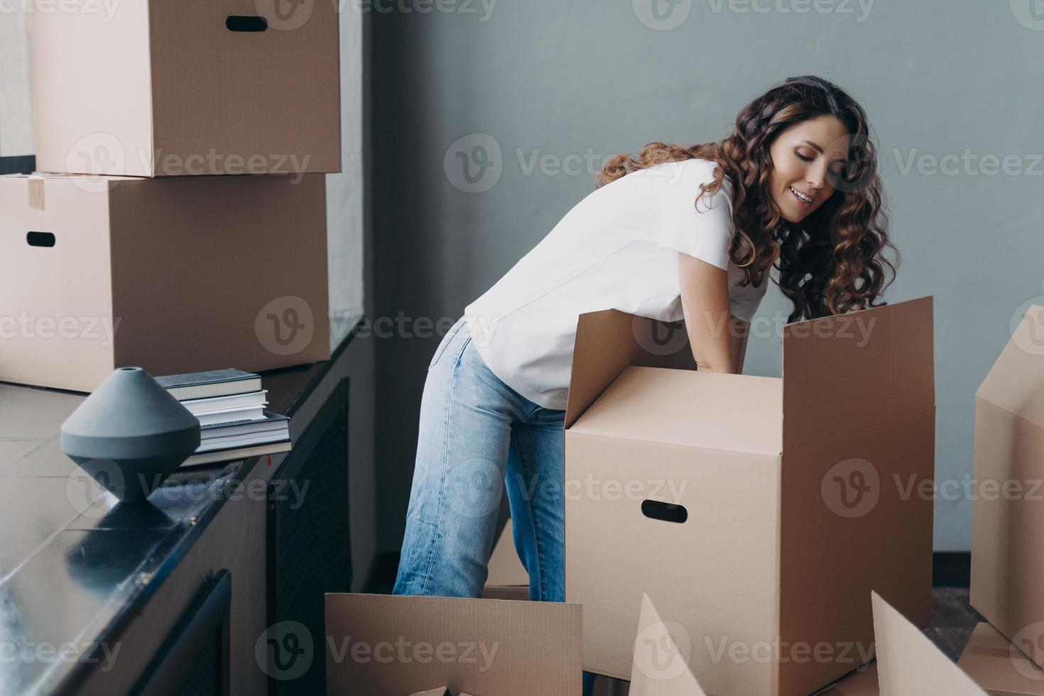 Hispanic woman unpack boxes with delivered things during relocation at new home. Moving, delivery photo