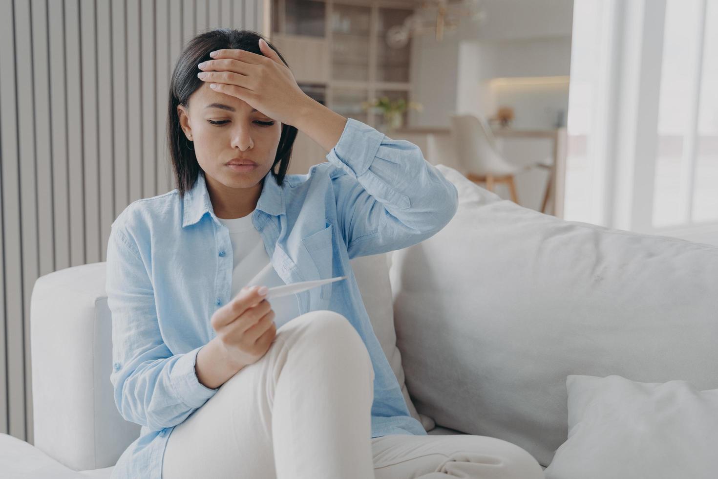 Unhealthy female holds thermometer, suffering from flu or coronavirus fever, high body temperature photo