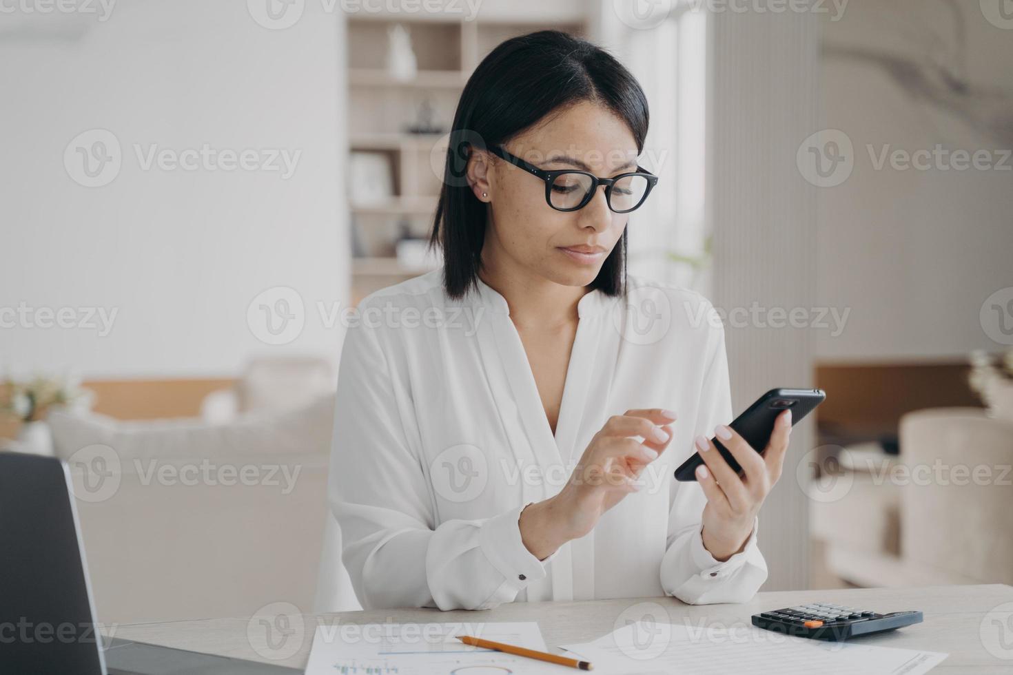 mujer de negocios con anteojos usando aplicaciones de teléfonos móviles para la gestión del tiempo de negocios sentada en una laptop foto