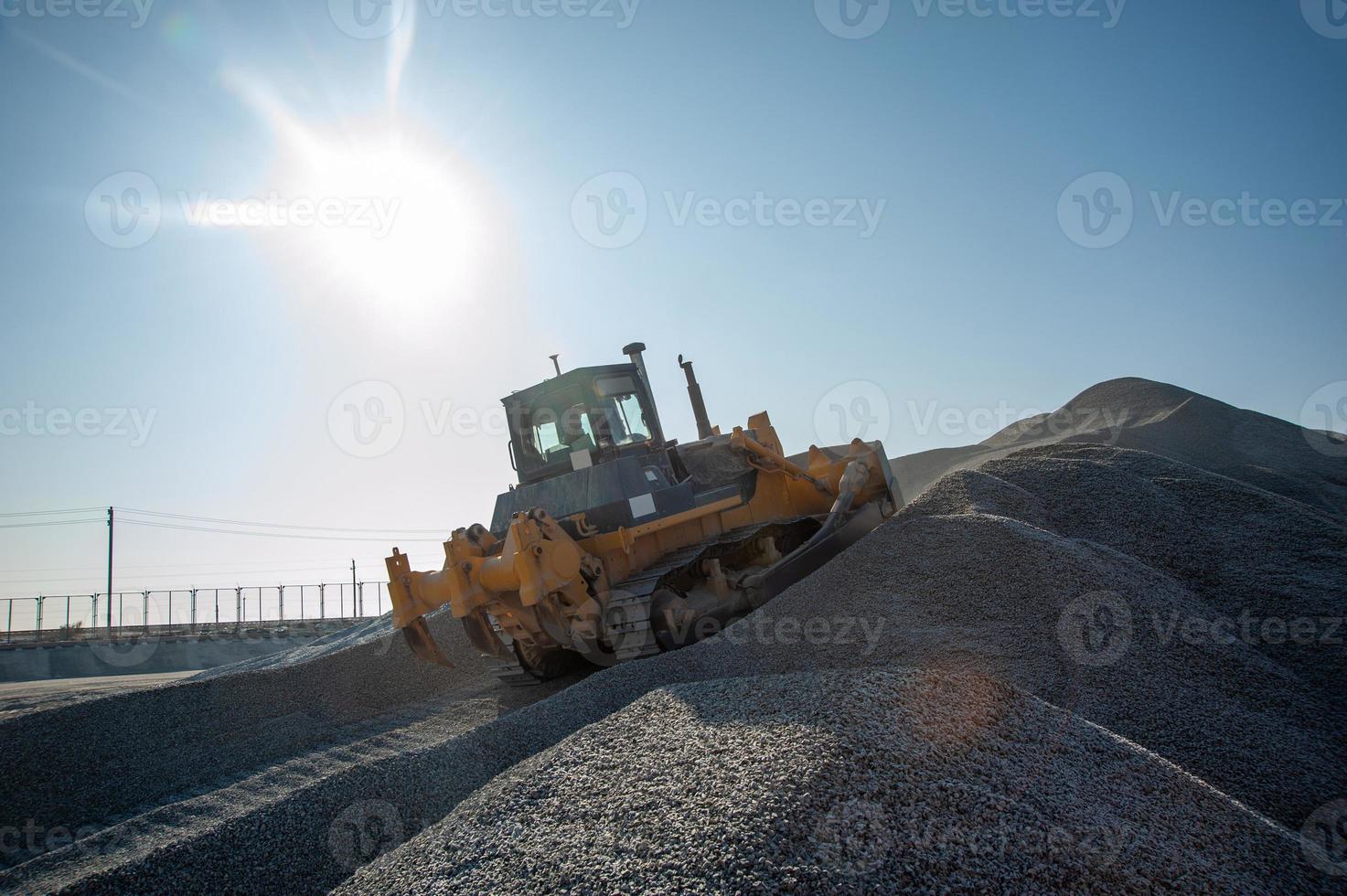 A heavy bulldozer on a mountain of gravel loading against sunny sky photo