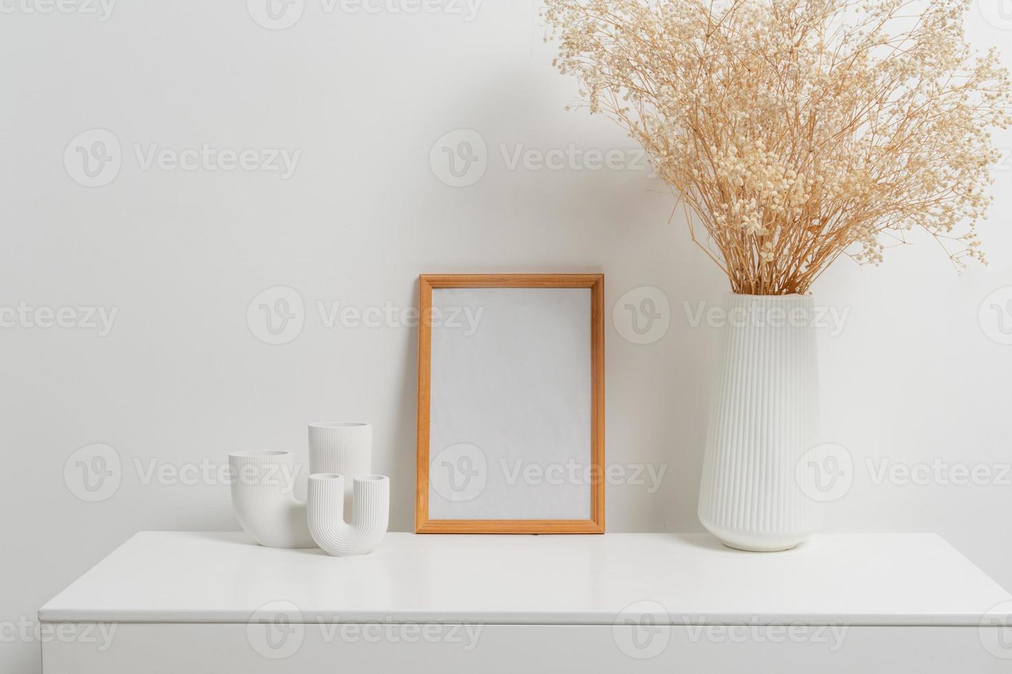 Wooden vertical frame with white vase of gypsophila flowers over white wall photo