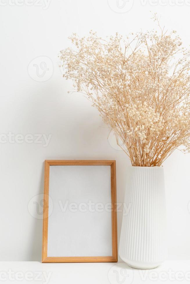 Wooden vertical frame with white vase of gypsophila flowers over white wall photo