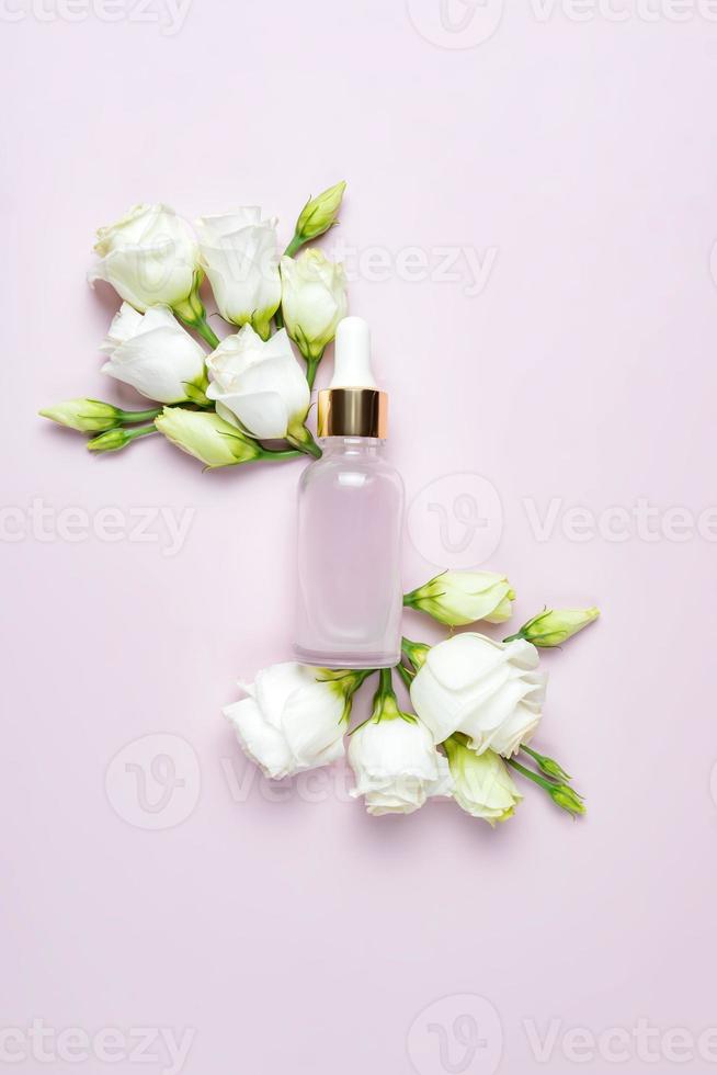 Tio view of beauty face serum in a glass dropper bottle on pink background with eustoma flowers. Skin care routine mockup package photo