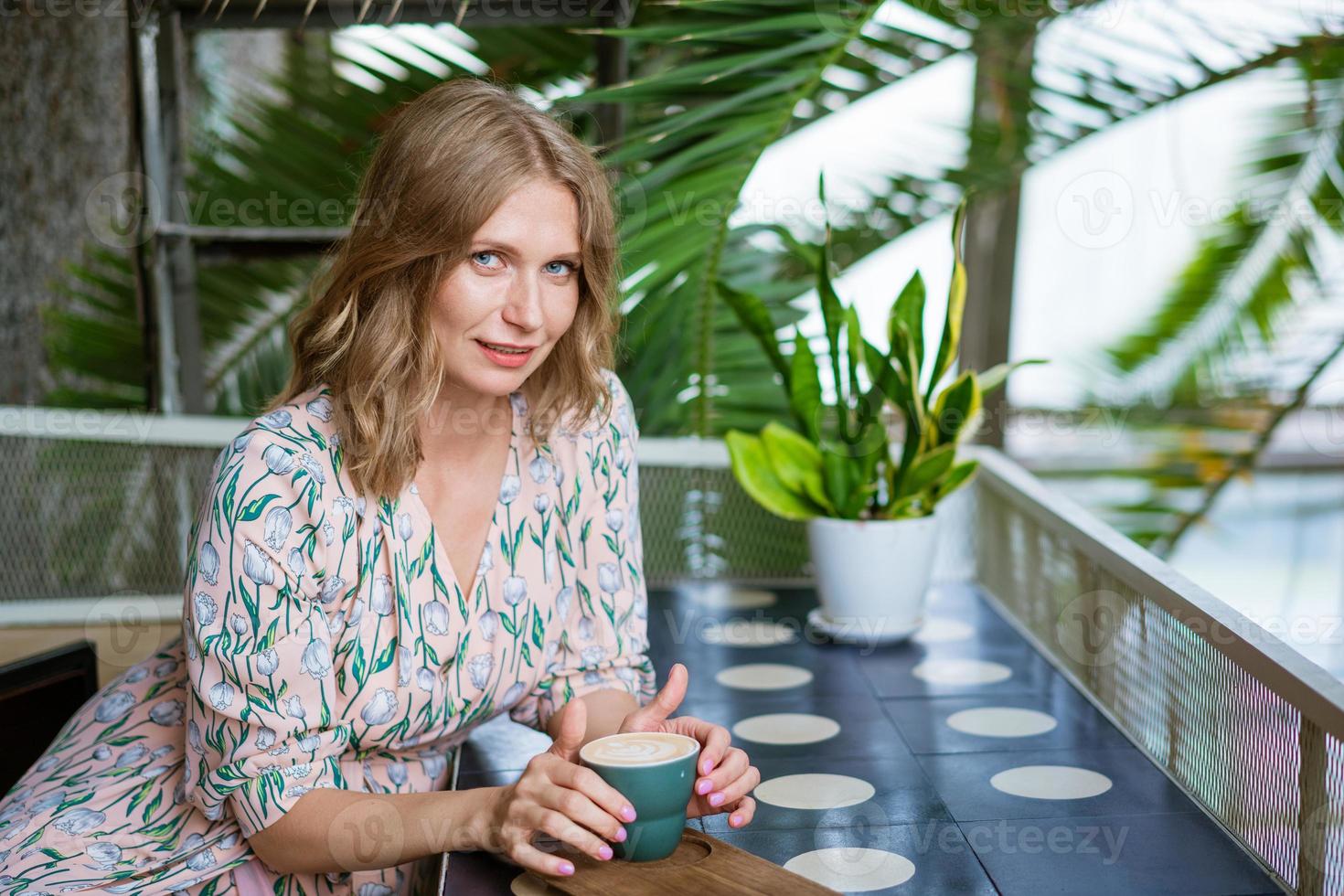 Happy smiling middle aged woman sitting in cafeteria holding coffee mug looking photo