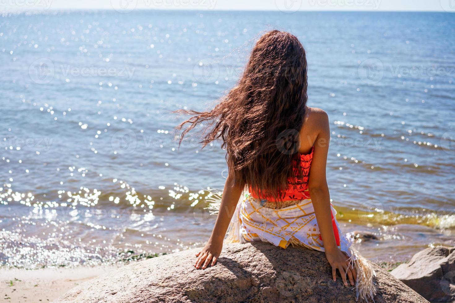 Beautiful slender young woman with wavy long hair sits on seashore on large photo