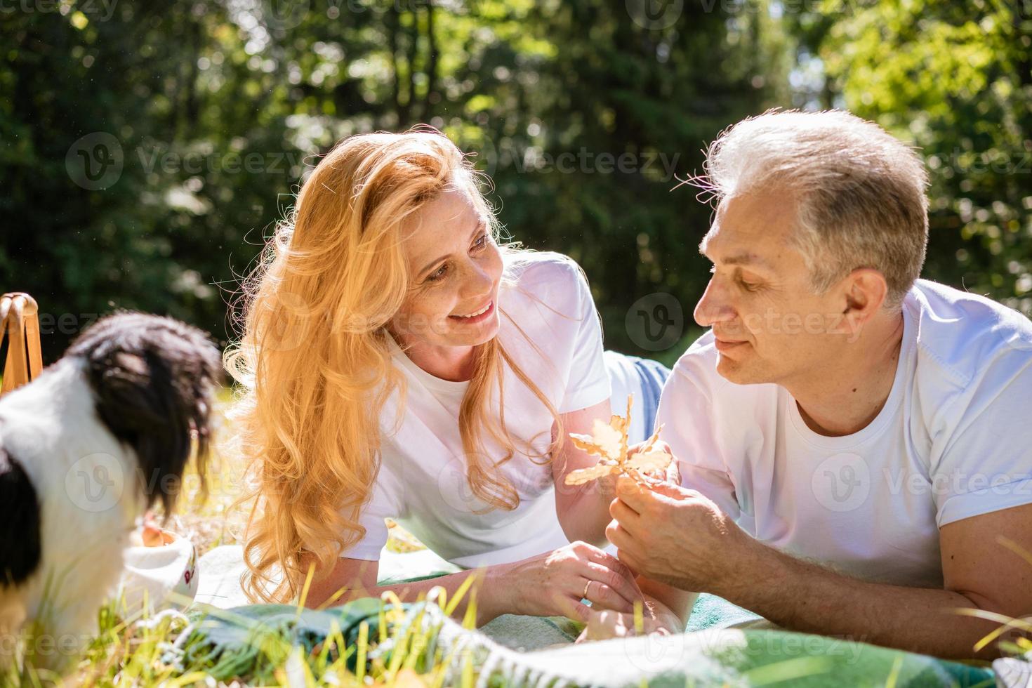 Mature couple lie with their dog in park. An elderly couple is resting photo