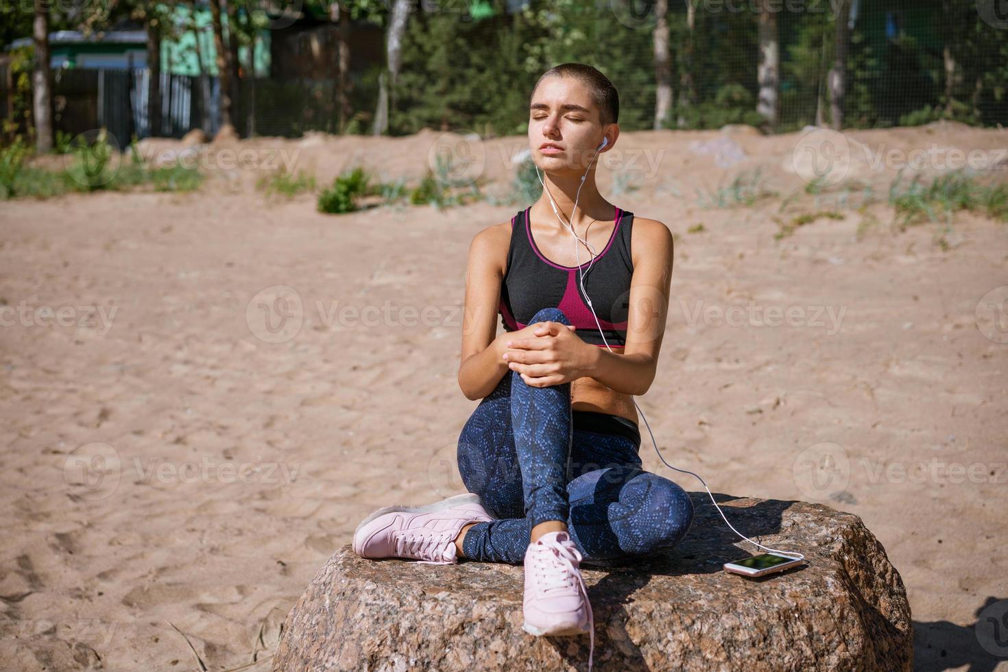 una joven vestida con ropa deportiva se sienta en la playa para aprender a escuchar música foto