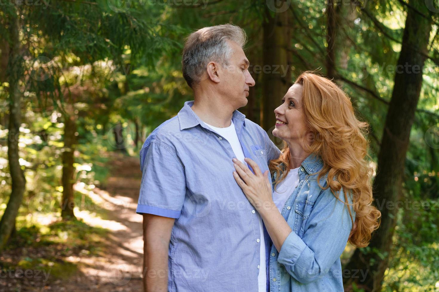 Smiling senior couple standing in park hugging each other together and smiling photo