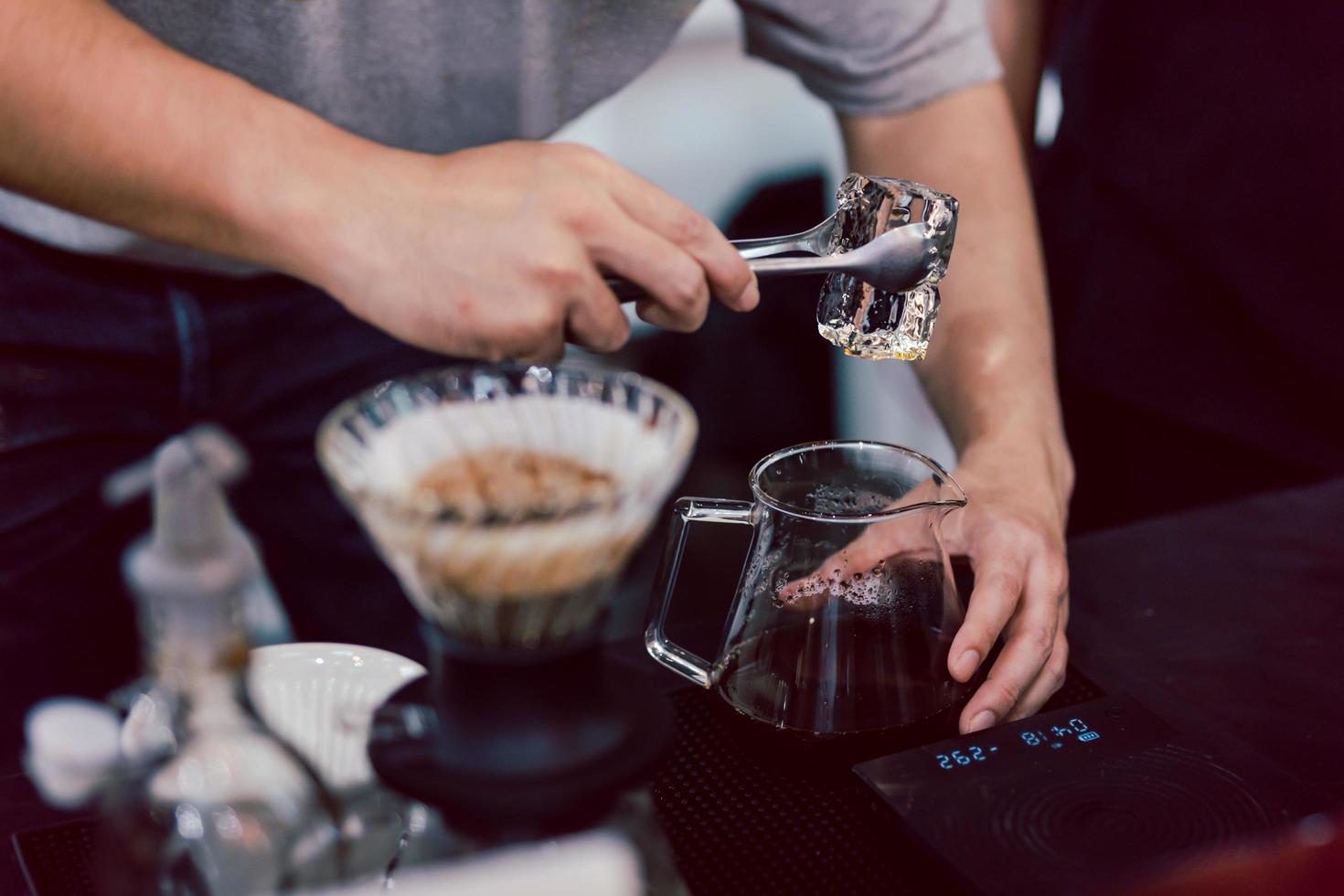 Barista making iced coffee by putting an ice into a glass jar with black freshly brewed coffee. photo