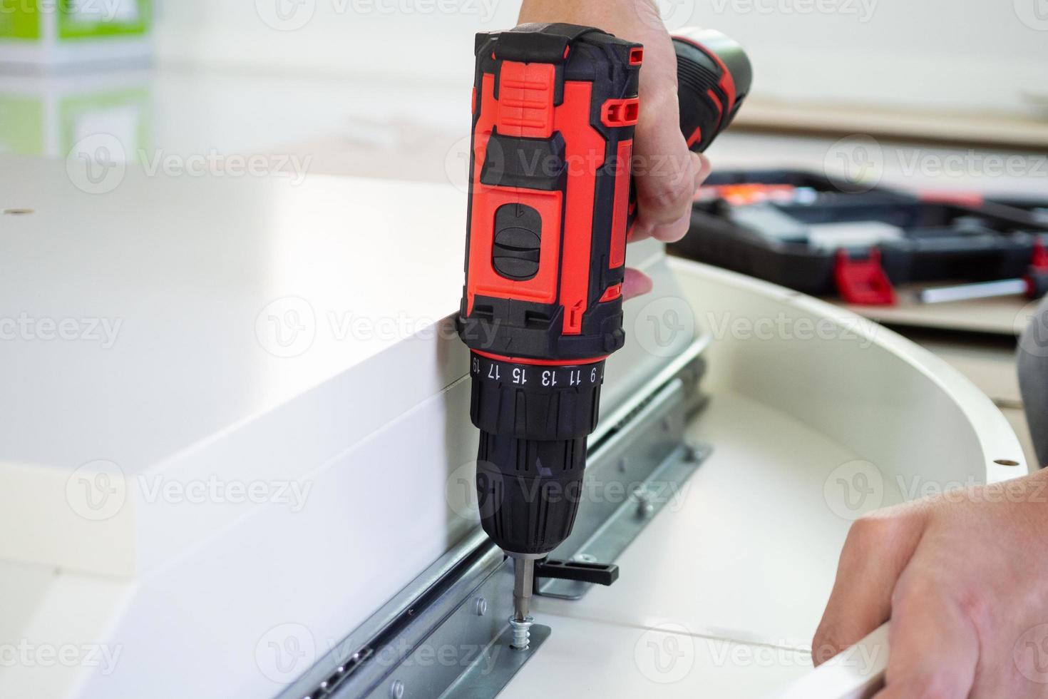man assembling white table furniture at home using cordless screwdriver photo