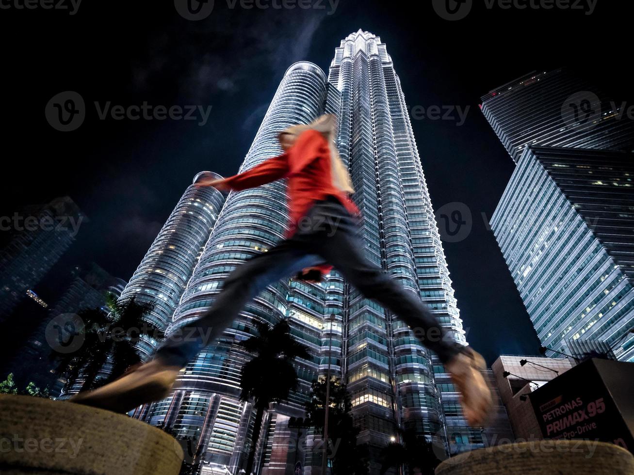 Low angle view of a girl in red jumping infront of the Petronas Twin Towers at night photo