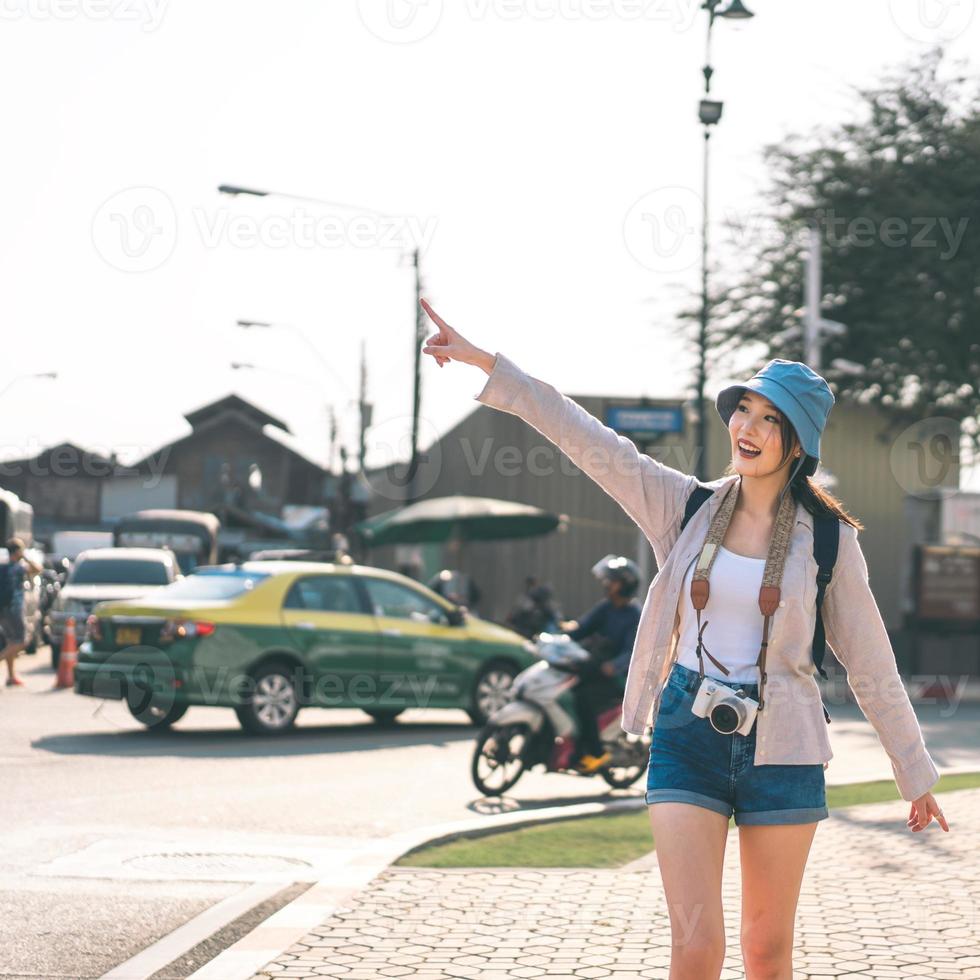 Walking young adult southeast asian woman traveller wear blue hat and backpack under sunlight photo