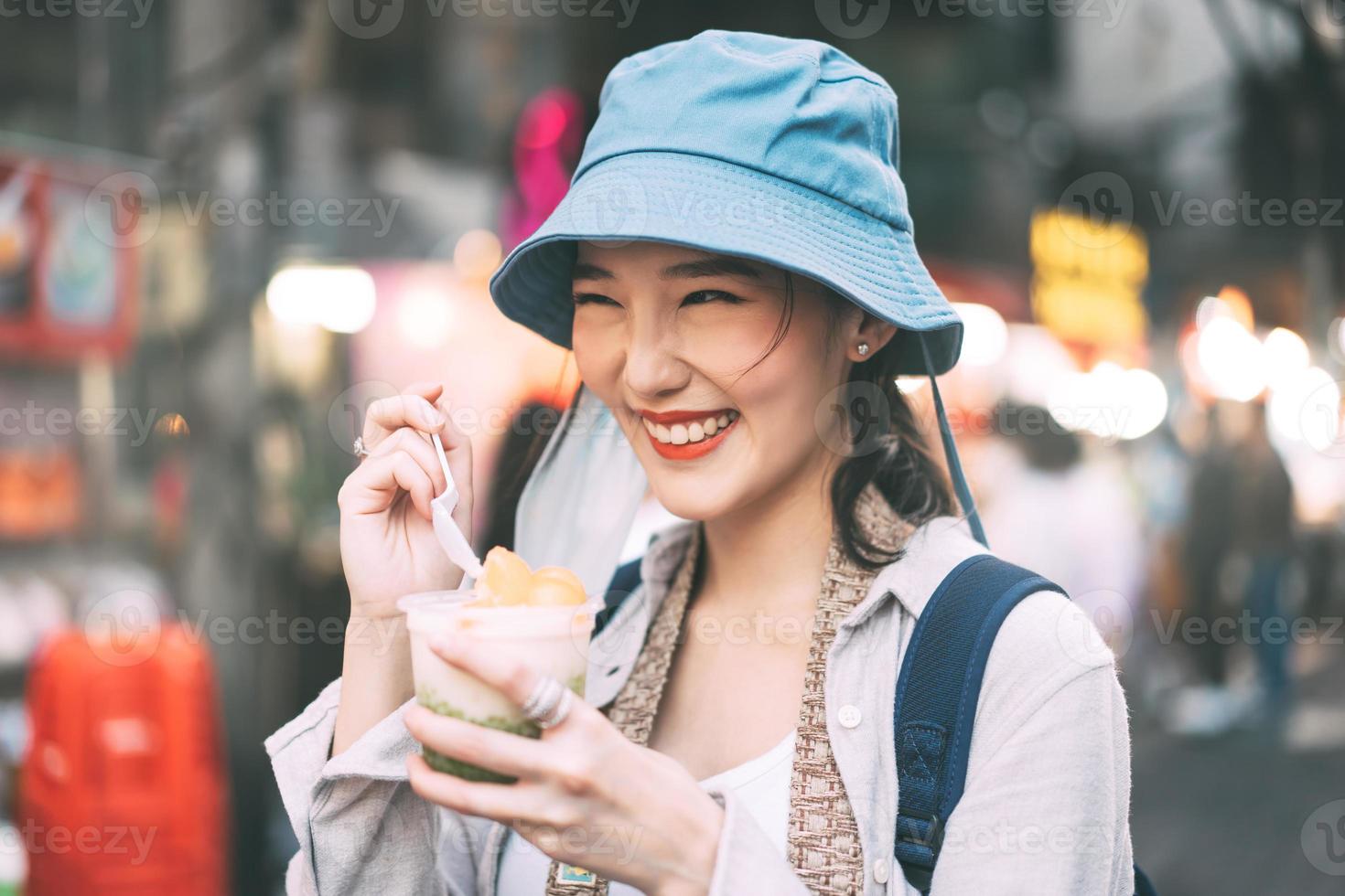 Young adult asian foodie woman backpack traveller eating asia dessert at chinatown street food. photo