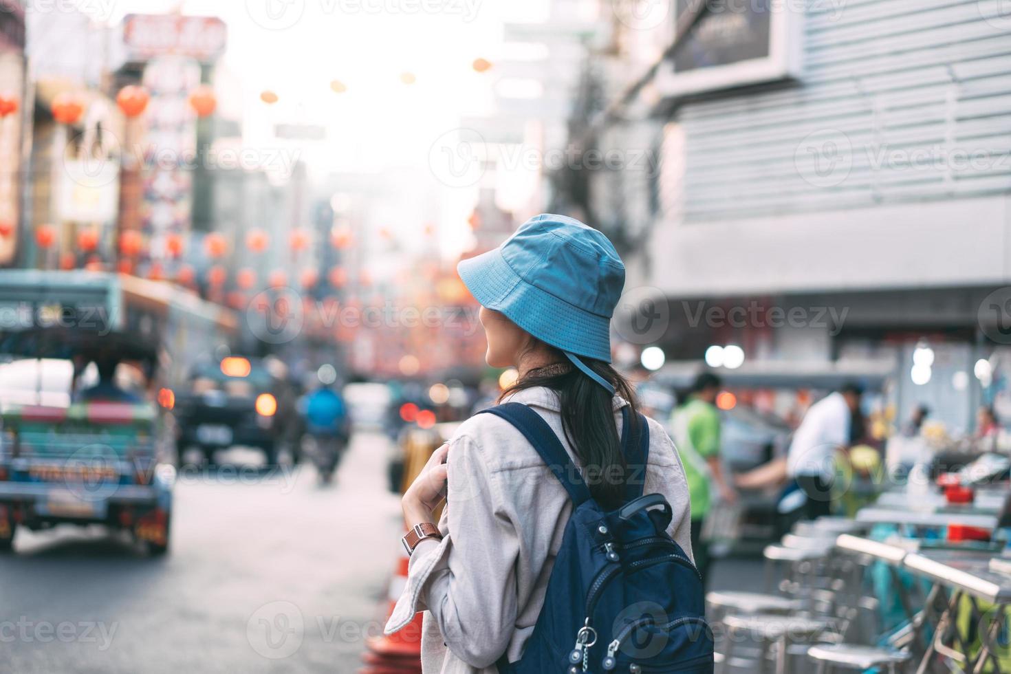vista trasera de la mochila de viajero de una joven adulta asiática caminando en la ciudad en el mercado nocturno de la calle. foto