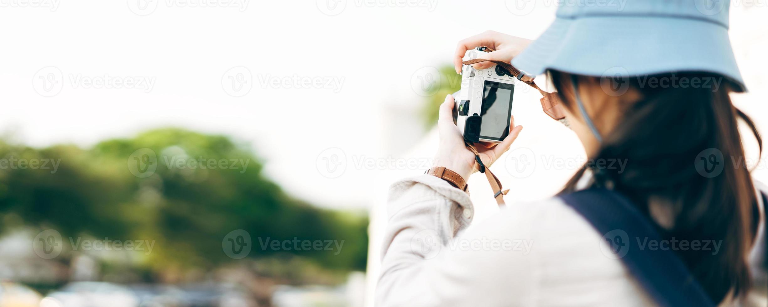 Rear view of young asian woman traveller using camera for travel banner size background. photo
