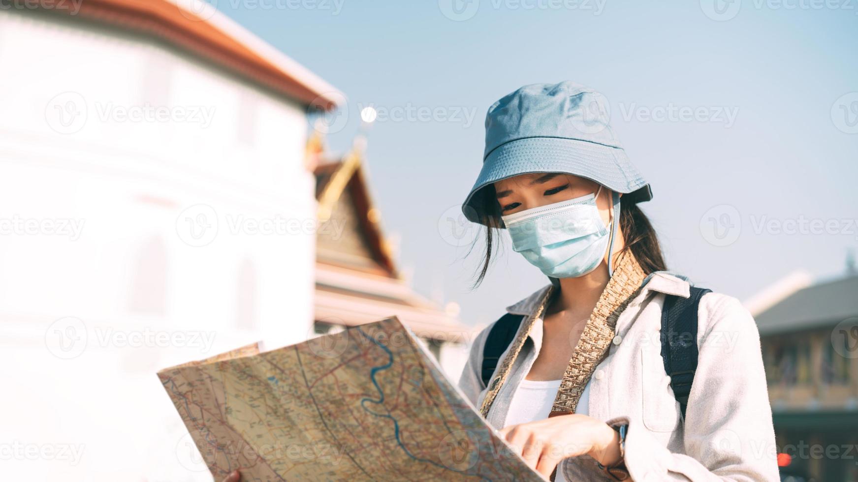 viajera adulta mujer asiática usa mascarilla para proteger el virus corona o covid 19 usando el mapa para buscar destino. foto