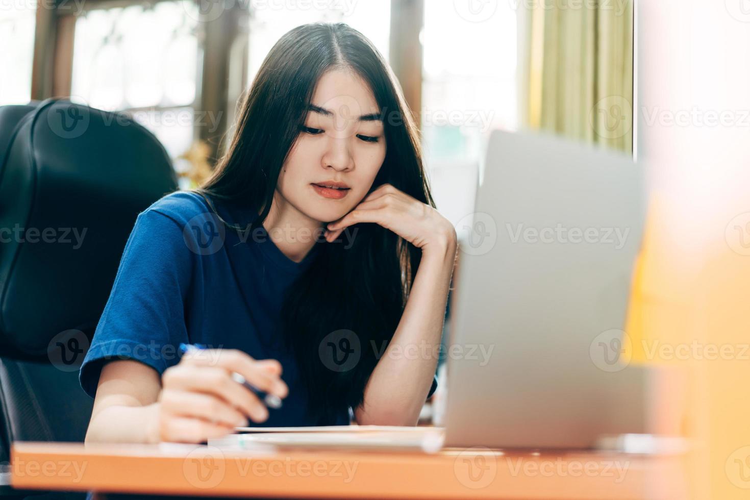 Young adult freelancer asian woman using laptop and write in home office photo