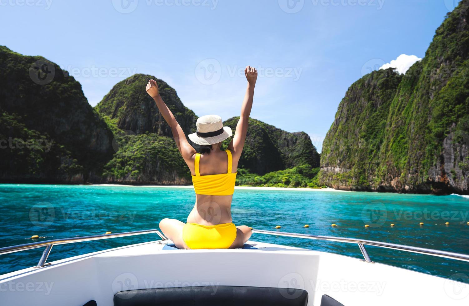 Vista trasera de una mujer viajera adulta que se relaja estirando el brazo en el velero con isla de verano y mar foto