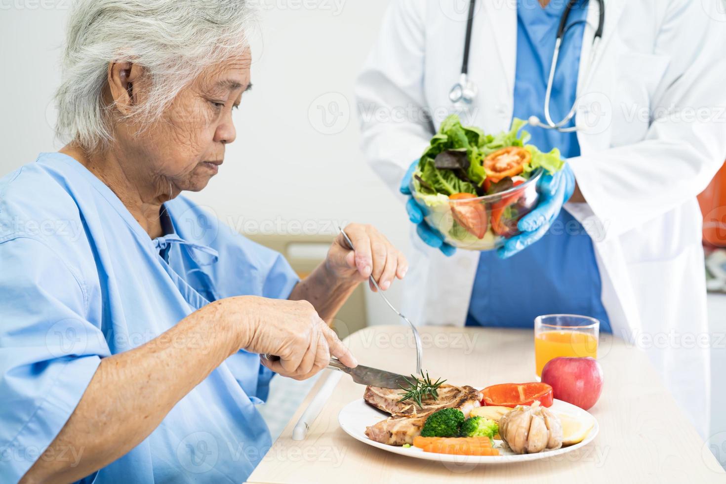 Asian senior or elderly old lady woman patient eating breakfast and vegetable healthy food with hope and happy while sitting and hungry on bed in hospital. photo