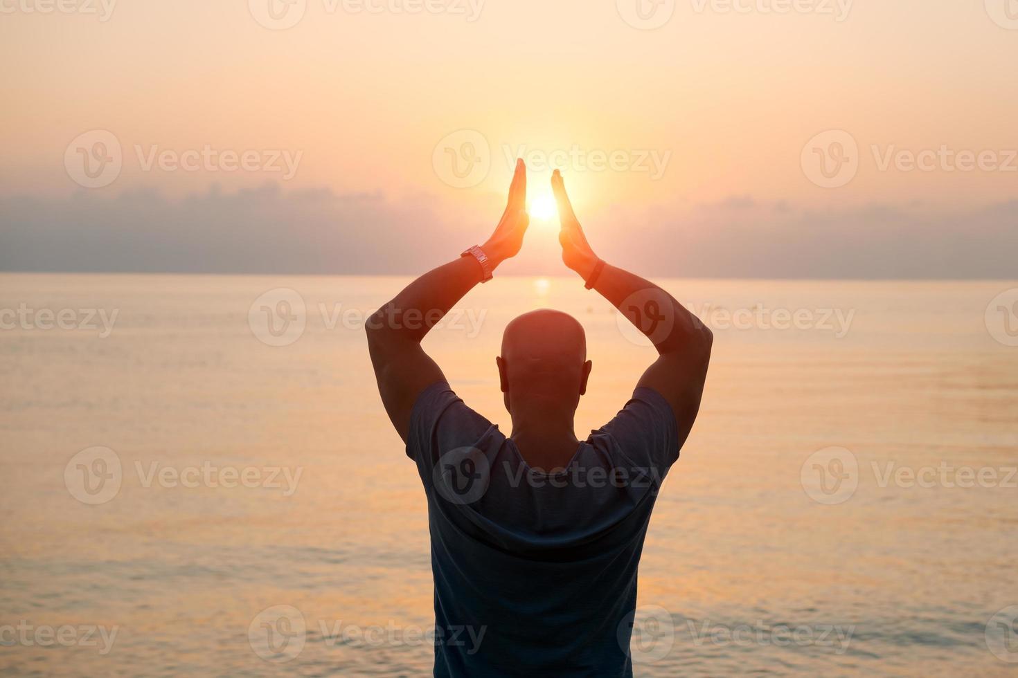 Silhouette man with his hands raised at sunset on beach arms out to sides photo
