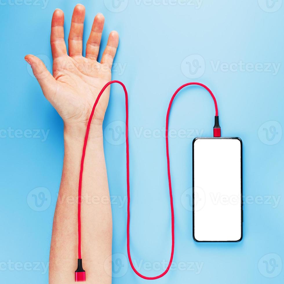 la mano está conectada por un cable de alimentación rojo a un teléfono inteligente con espacio libre en un fondo azul. foto