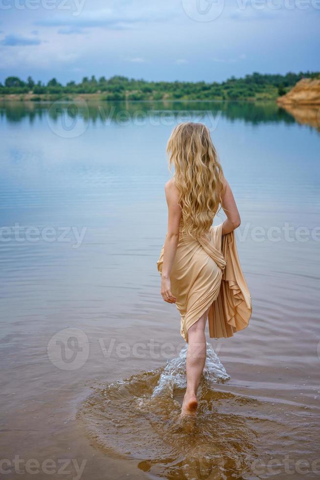 A beautiful slender young woman in a long dress stands in the water in the lake photo