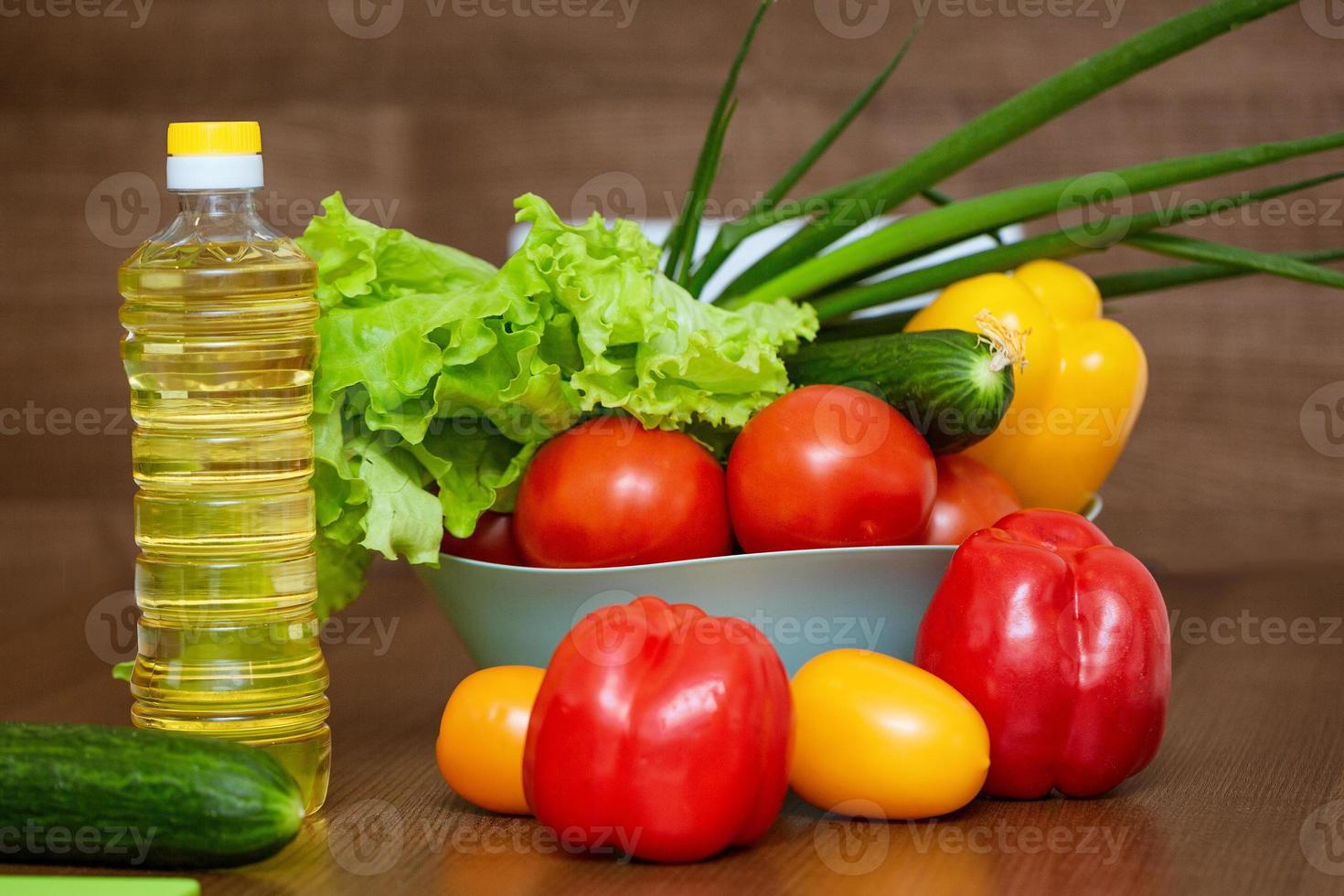 Fresh vegetables in a bowl on a wooden table and a bottle of oil photo