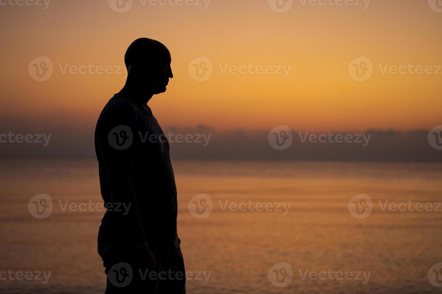 Male silhouette on background sea at sunset looks to side alone. Man enjoying photo