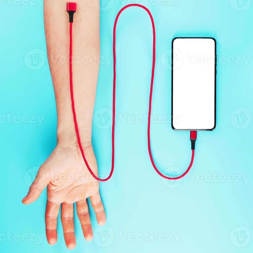 la mano está conectada por un cable de alimentación rojo a un teléfono inteligente con espacio libre en un fondo azul. foto