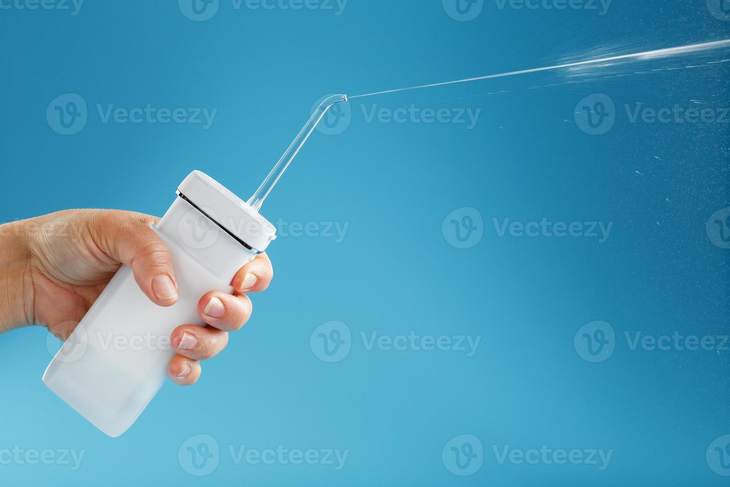 Irrigator in hand for cleaning the mouth with a shot of water jet on a blue background photo