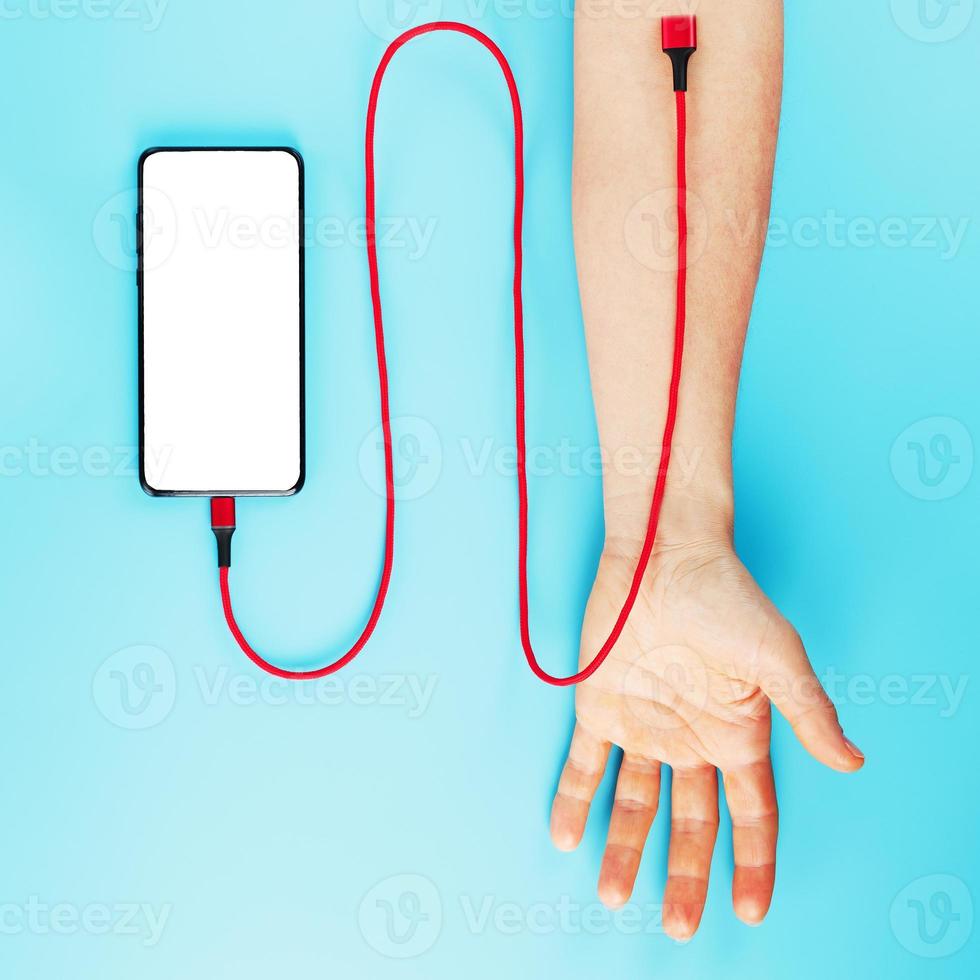 A smartphone with a large white screen is connected via a red USB cord to a vein in the hand on a blue background. photo