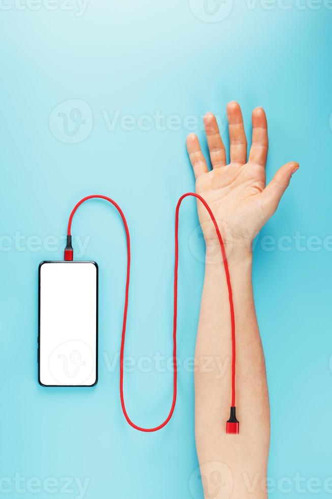 un teléfono inteligente con una gran pantalla blanca está conectado a través de un cable usb rojo a una vena en la mano sobre un fondo azul. foto