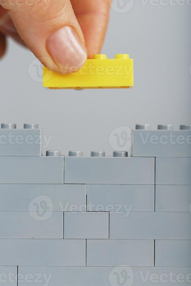 A gray wall made of a toy construction set with the last yellow brick in hand photo