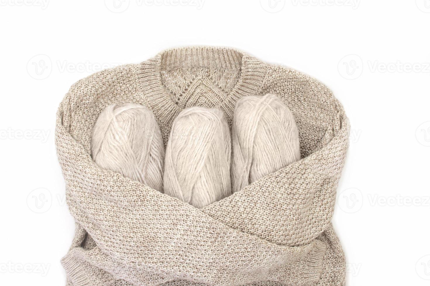Knitted sweater hugs skeins of yarn on white isolated background. Concept of knitting, sewing. Copy space photo