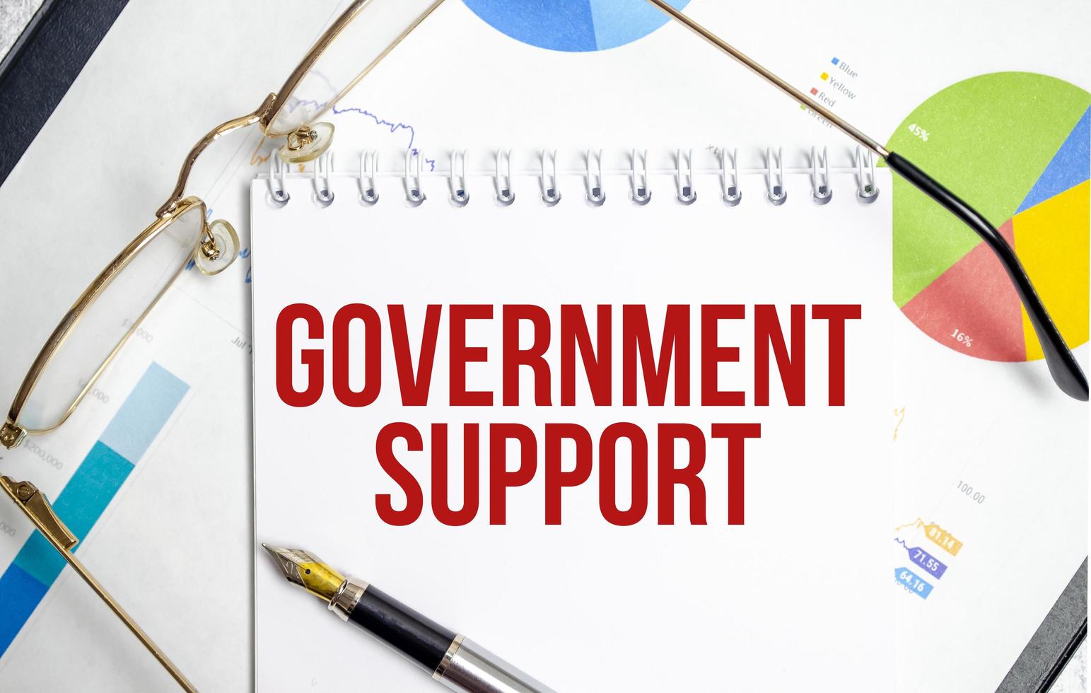government support text written on white notebook with calculator and pen photo
