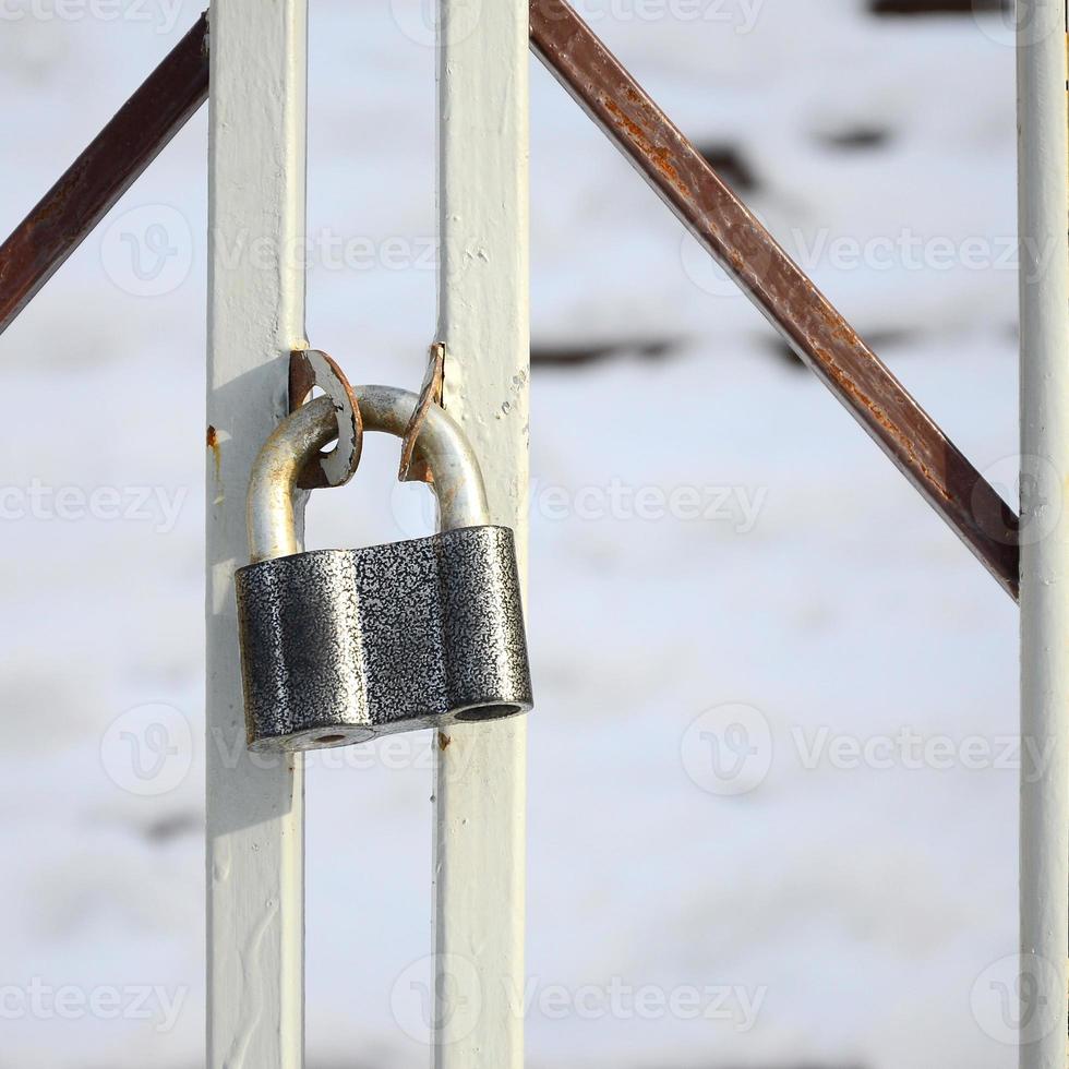 A large gray padlock hangs on a metal gate photo