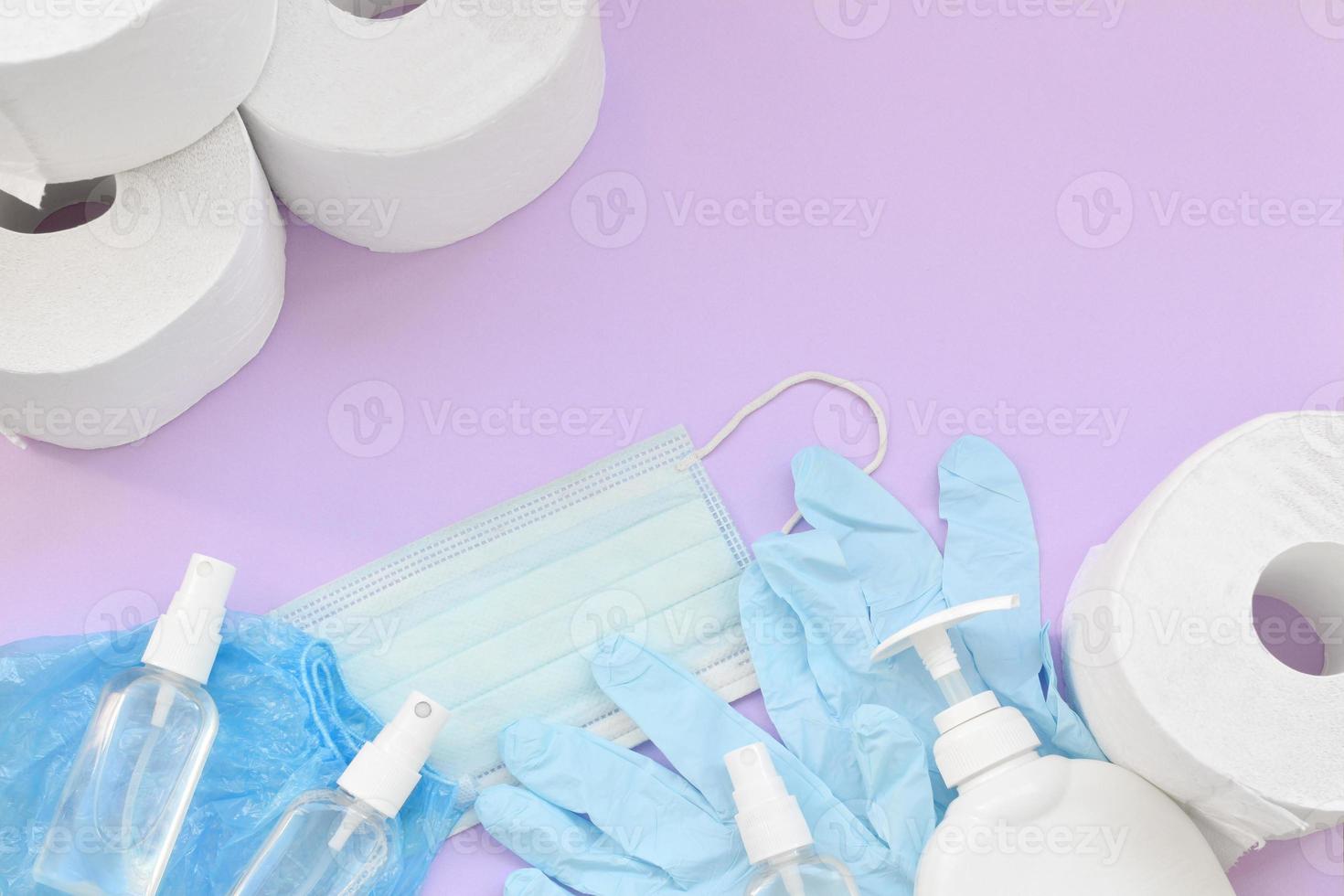 Set of important items for Covid-19 quarantine. Toilet paper, rubber disposable gloves with surgical face mask and hand sanitizer with liquid soap bottle on lilac background photo