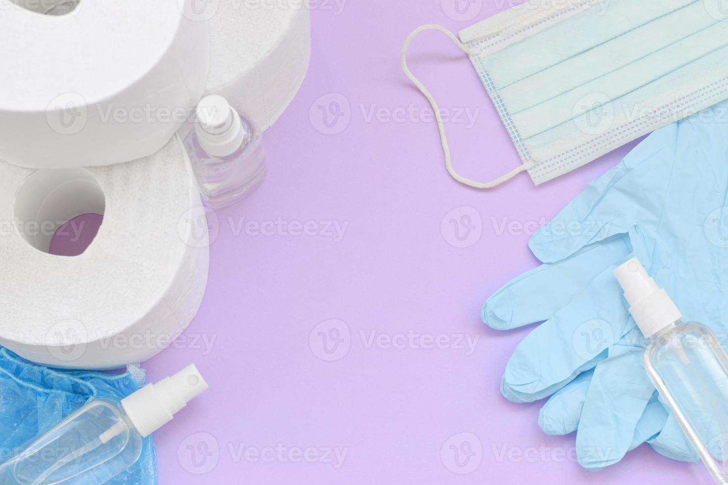 Set of important items for Covid-19 quarantine. Toilet paper, rubber disposable gloves with surgical face mask and hand sanitizer on lilac background photo