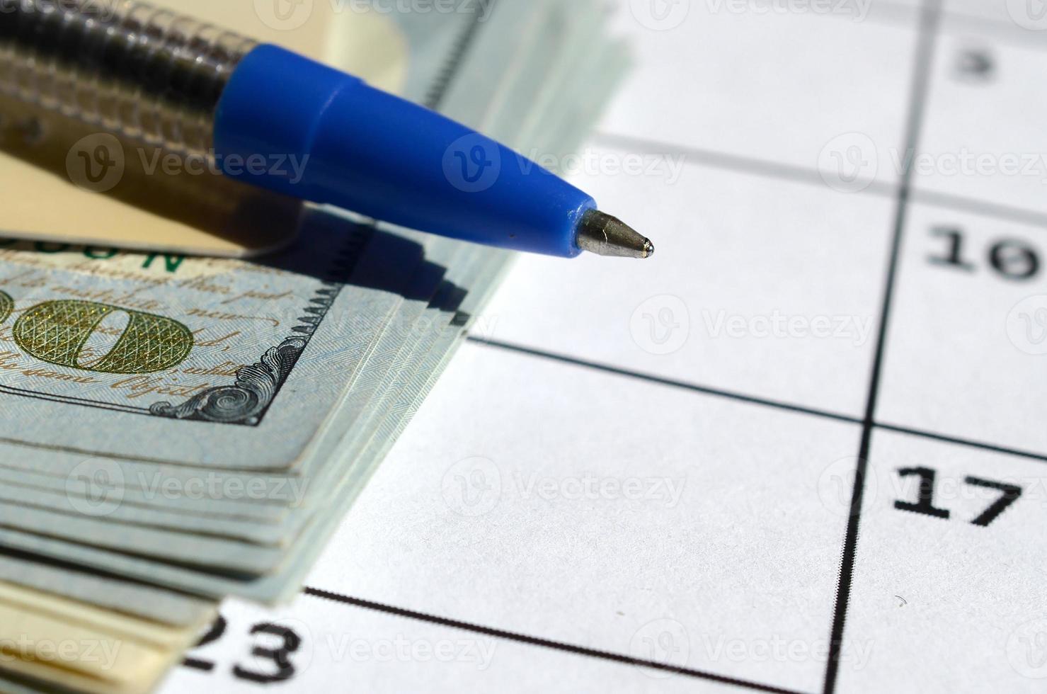 Pen and credit card on many hundred US dollar bills on calendar page close up photo