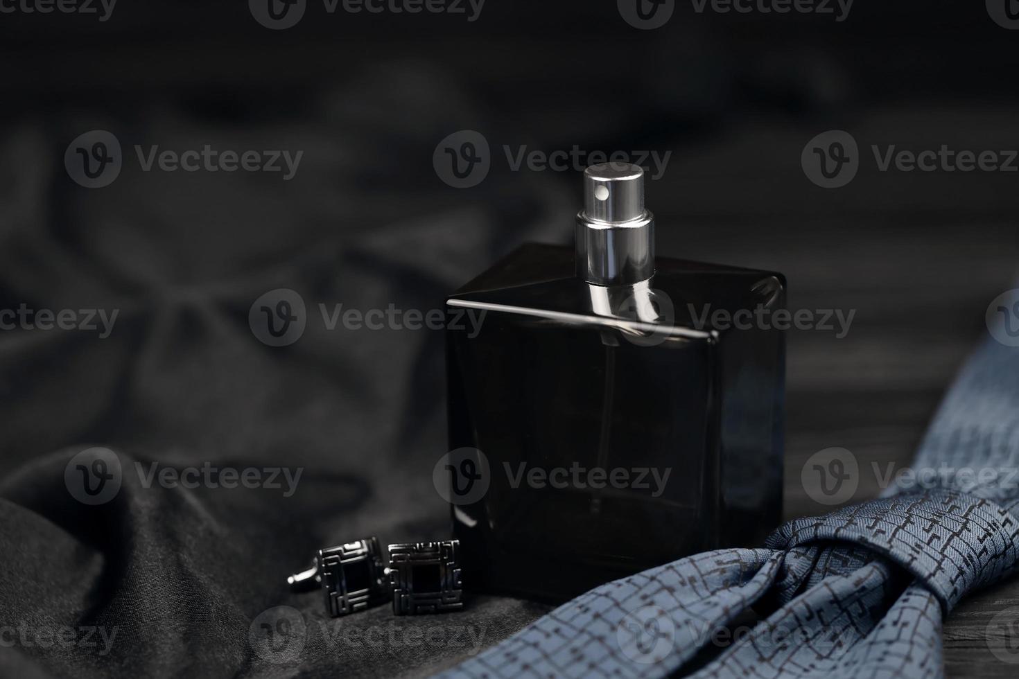 A bottle of mens cologne and cufflinks with blue tie lie on a black luxury fabric background on a wooden table. Mens accessories photo